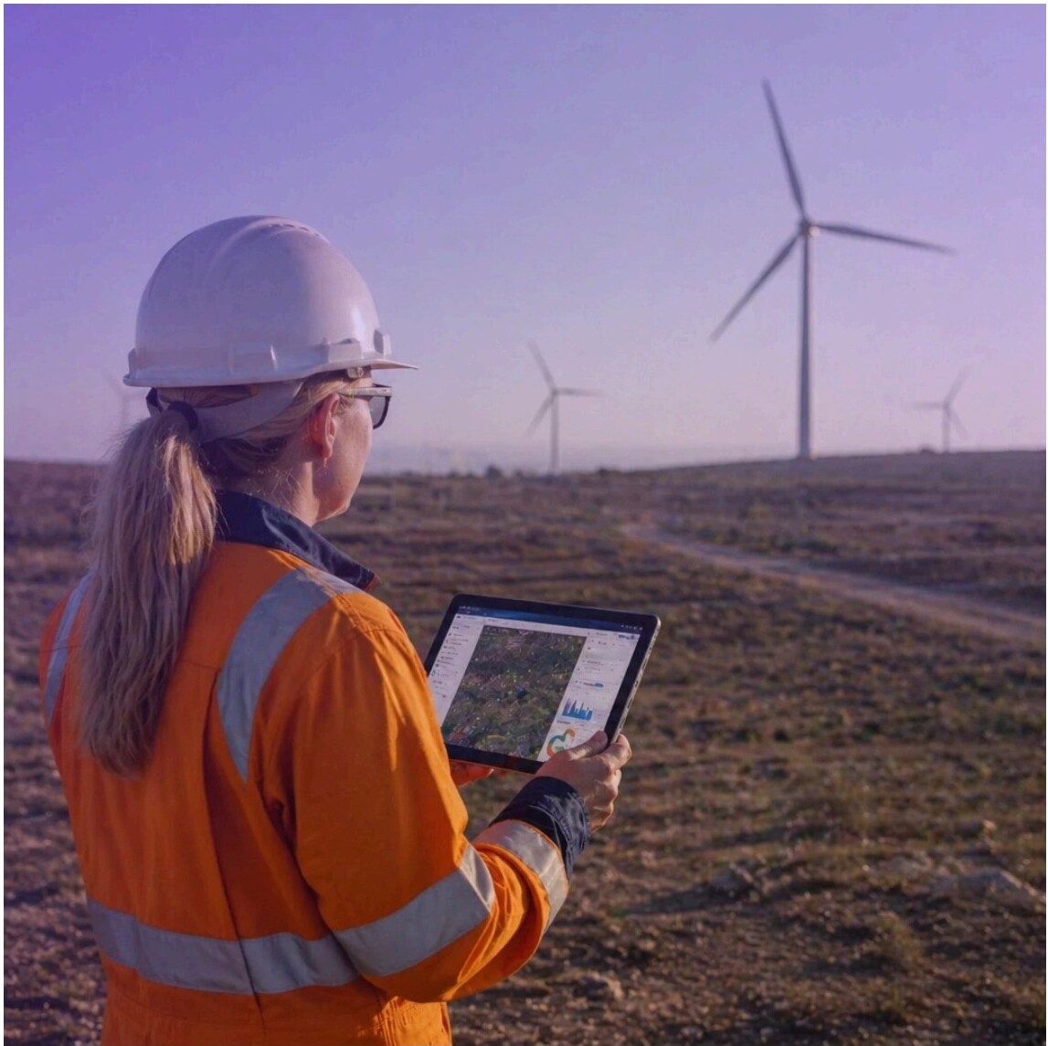 Worker in hard hat holding tablet, wind turbines in the background